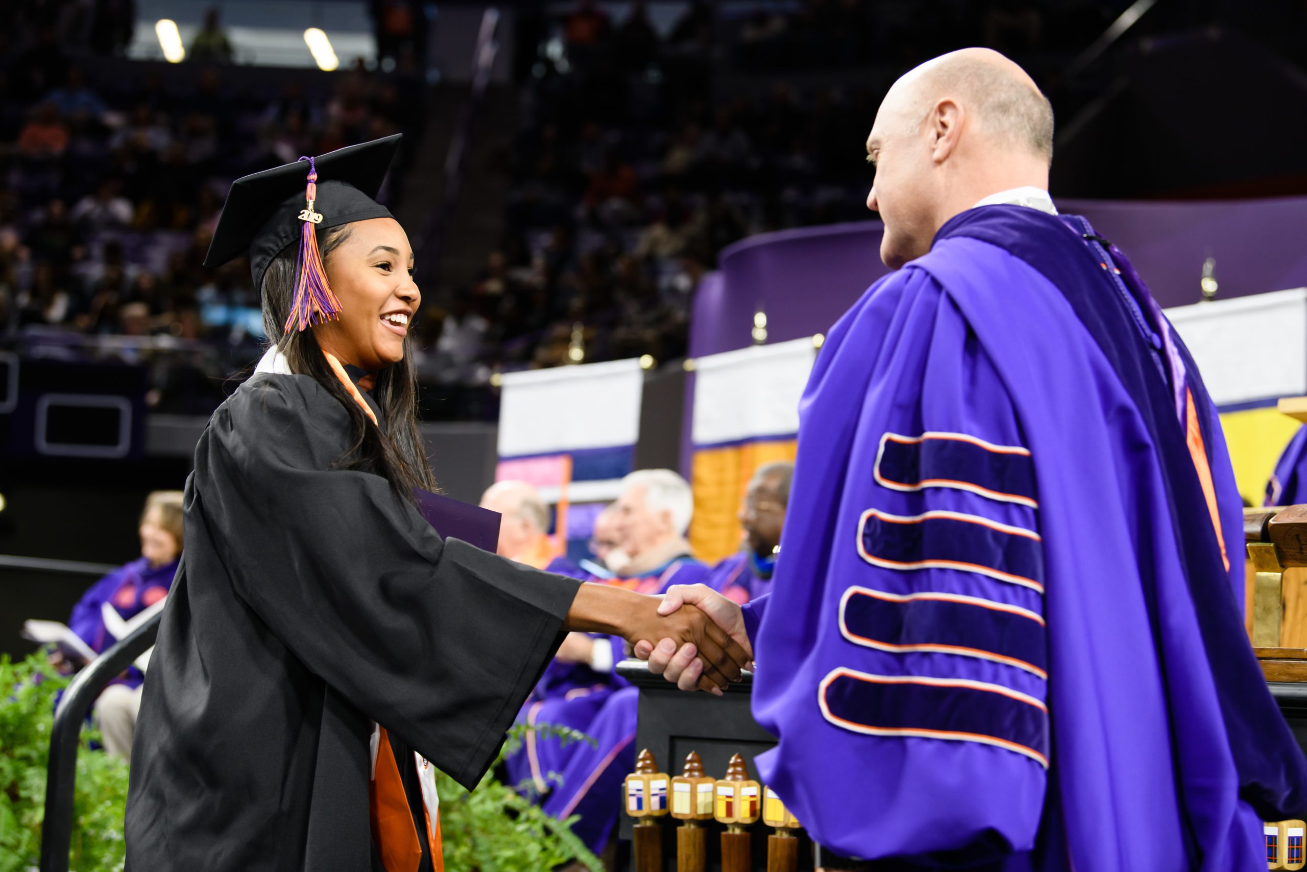 President Clements on stage at graduation shaking hands with a female student graduating.