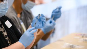 Nurses wearing gloves preparing a needle with the vaccine.

