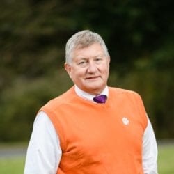 Man in white shirt with orange pullover vest standing outside