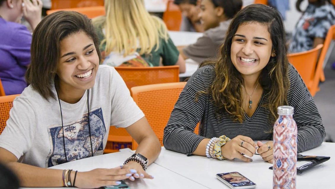 Two female students sit at a table, laughing