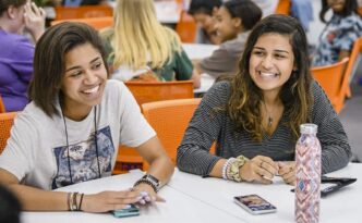 Two female students sit at a table, laughing