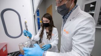 CECAS student Lauren Slann in the lab wearing white coat and making measurements.