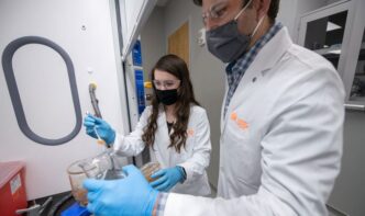 CECAS student Lauren Slann in the lab wearing white coat and making measurements.