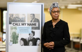 Photo of Rhondda Thomas next to a sign about "Call My Name" exhibition.