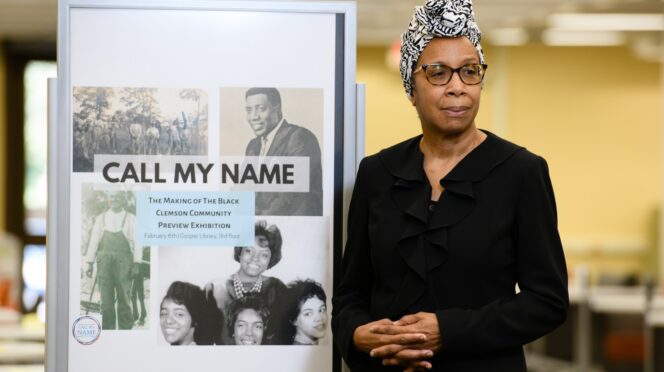 Photo of Rhondda Thomas next to a sign about "Call My Name" exhibition.