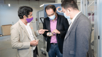 Three men in suits looking at composite printed structure in lab.