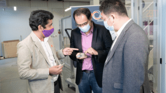 Three men in suits looking at composite printed structure in lab.