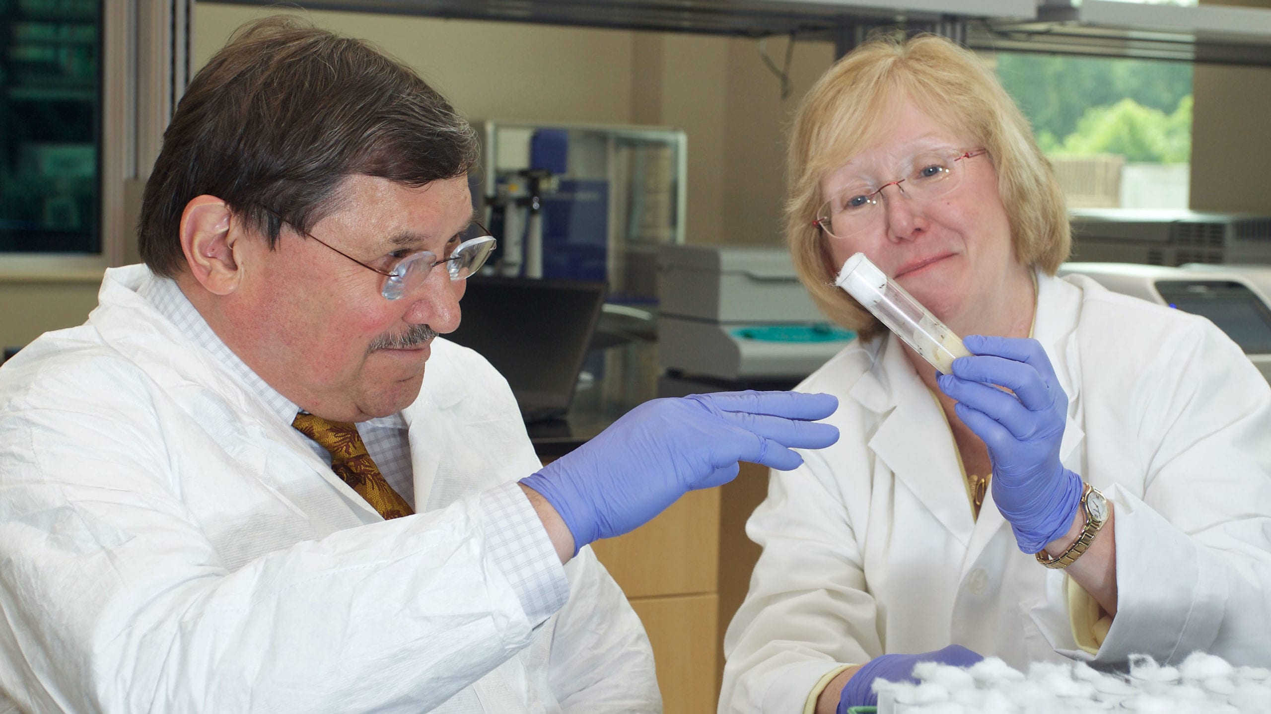 Robert Anholt and Trudy Mackay in a lab holding a test tube with fruit flies inside