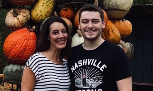 Mother and son arm in arm and with face masks in hands while standing in front an autumn display of pumpkins.