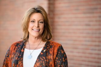 Tax season expert Lynn Martin, woman who gave tax filing and tax return tips for taxpayers, smiling and standing in front of a brick wall on the outside of the business school.