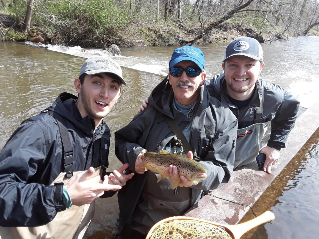 picture of three men standing in a stream and holding a fish