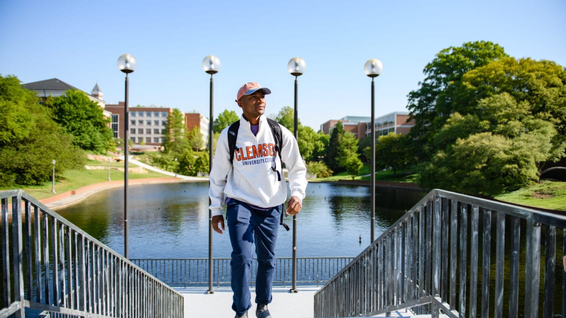 Man in Clemson sweatshirt walks up stairs in front of reflection pond