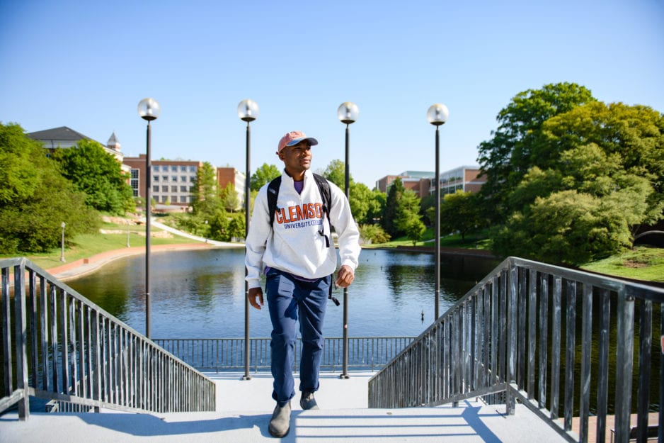 Man in Clemson sweatshirt walks up stairs in front of reflection pond