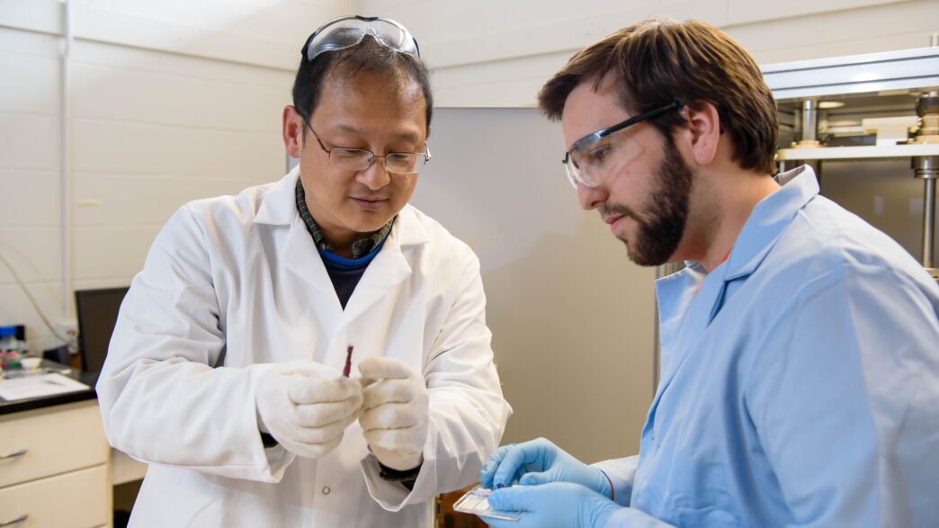 man in white lab coat how's man in blue lab coat something in a science lab
