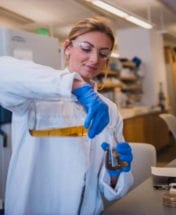 woman wearing white lab coat pouring something in a lab