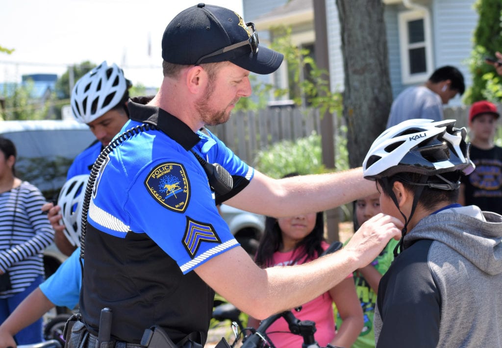 MTSA student Brian Cluever, a commander with the Carol Stream Police Department in Illinois, showing children the correct way to wear helmets. This relates to road safety in regard to bikes, skateboards and other hobbies and sports.