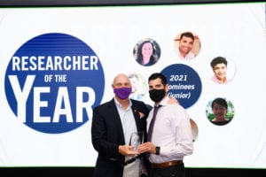Clemson University President Jim Clements, left, presents the junior Researcher of the Year award to Lior Rennert, right. Clements and Rennert are standing in front of a screen that displays a blue circle with the words "Researcher of the Year."
