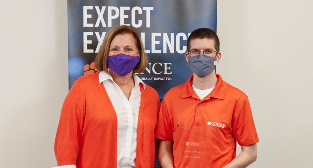 lady with orange suit coat standing next to man in orange polo shirt in front of a banner