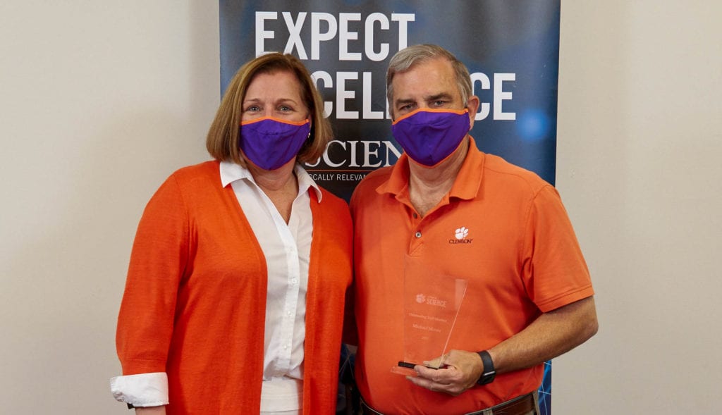 women wearing orange suit jacket standing with man wearing orange polo shirt in front of a banner