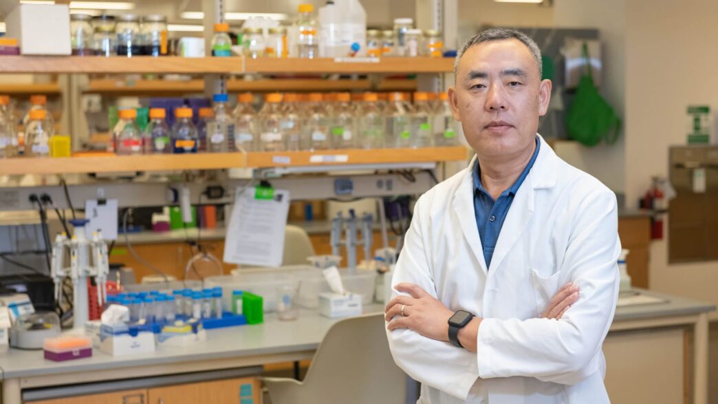 man in white lab coat standing in front of a table with test tubes
