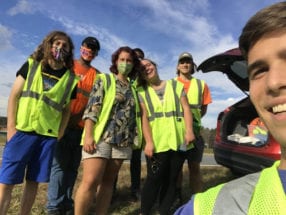 A selfie containing seven people in bright green security vests on the side of the highway.