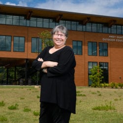 Woman standing outdoors in front of a modern wood building, soft clouds in the sky