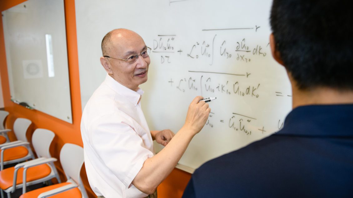 Professor Channing Tong writes equations on a white board for a student.