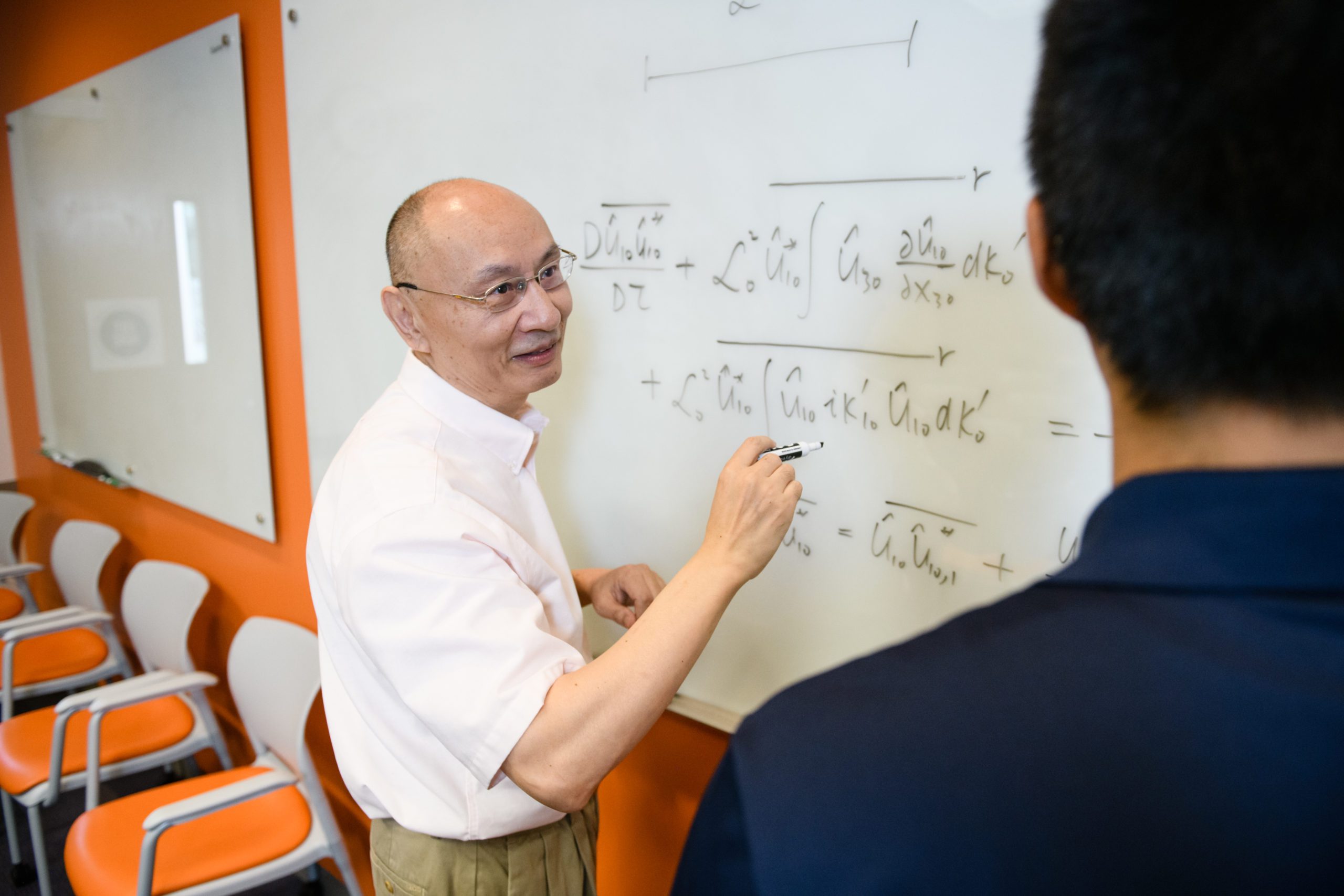 Professor Channing Tong writes equations on a white board for a student.