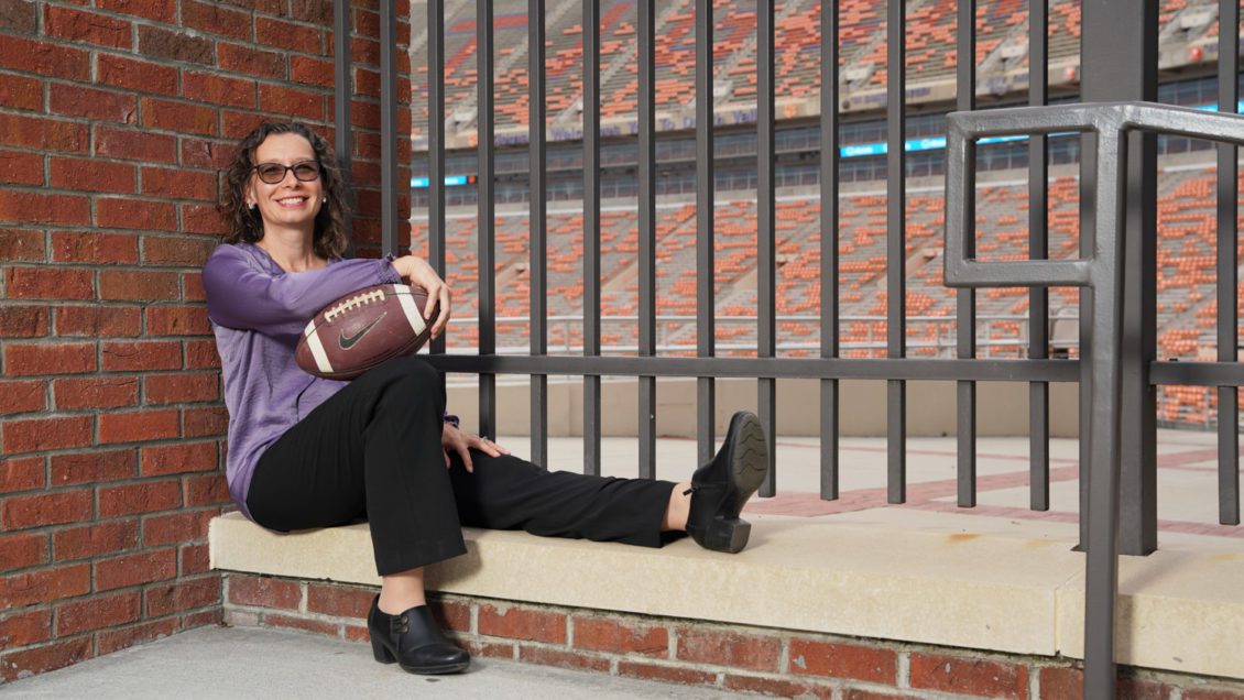 Woman holding a football sitting at a gate at Memorial Stadium