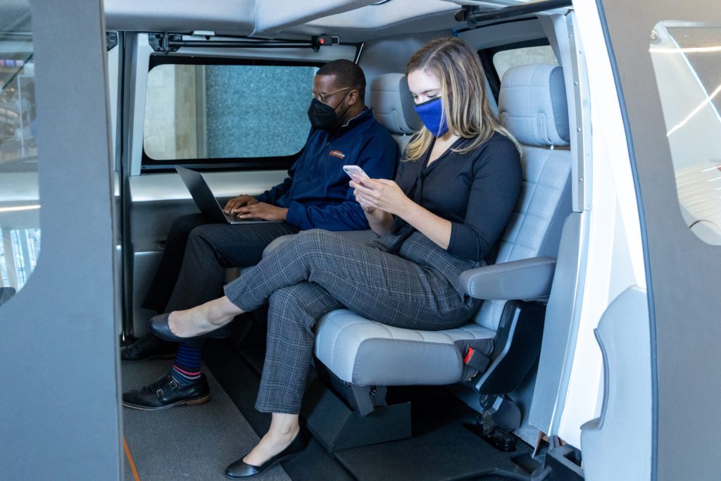 Two people sit comfortably in the inside of the car while looking at their devices. 