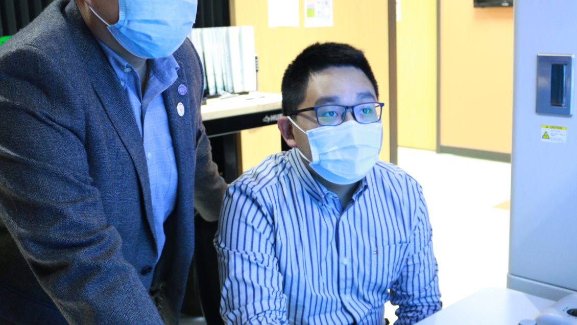 PhD student Hongkui Zheng, at right, works with faculty advisory Kai He in a microscope lab.