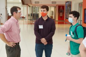 Man with a face shield talks to two students in a hallway