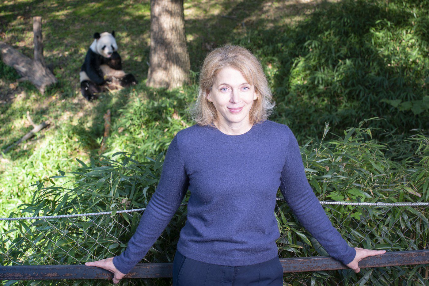 Portrait of Brandie Smith, wearing a blue shirt and standing in front of a panda exhibit at the zoo.