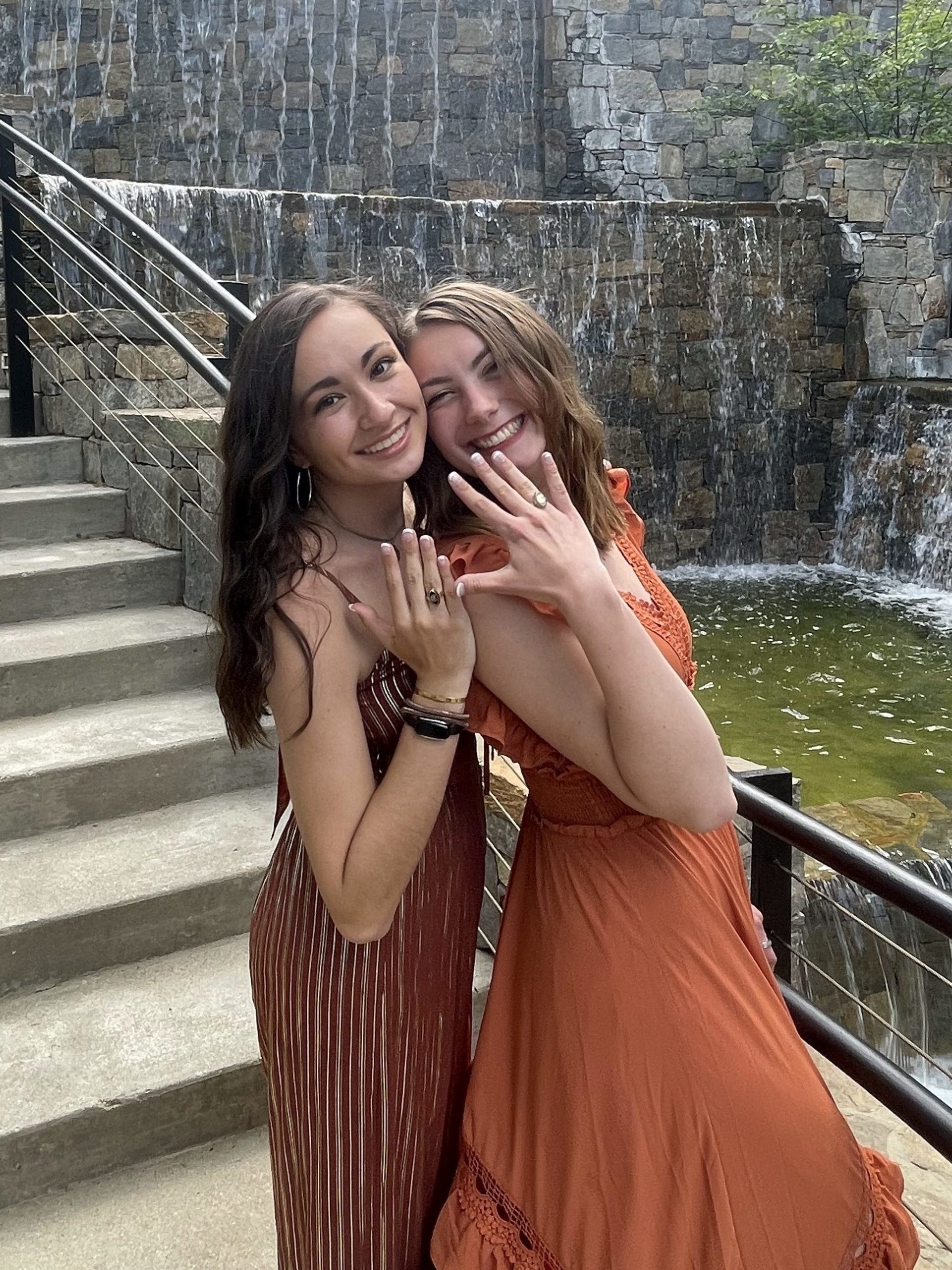 Two college seniors from Clemson showing their class rings in front of a waterfall