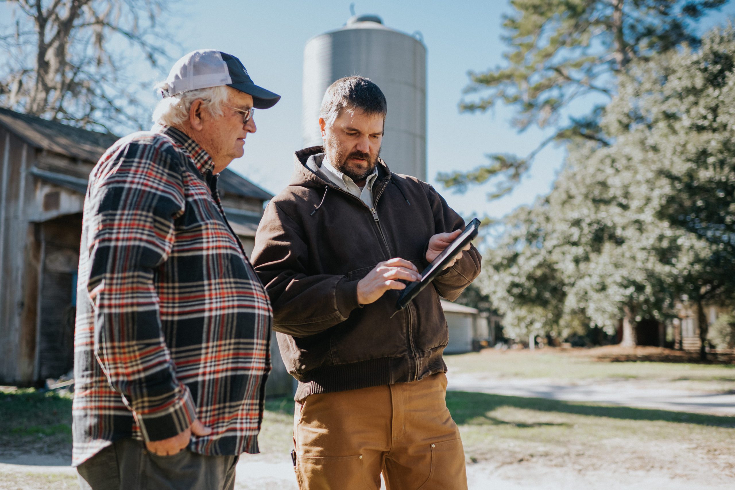 Bamberg County farmer Richard Rentz and Clemson precision agriculture engineer Kendall Kirk work with a tablet in front of a grain silo. 