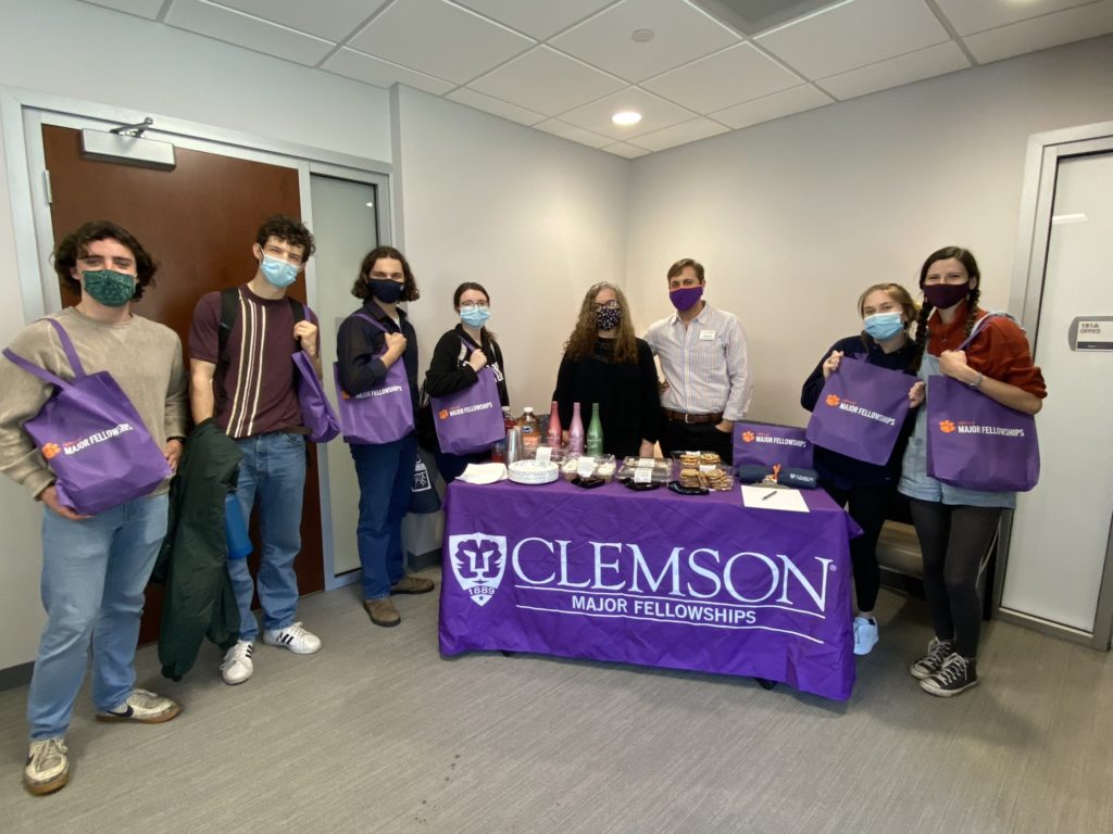 A group of people standing around a table at the major fellowships office and holding purple bags.