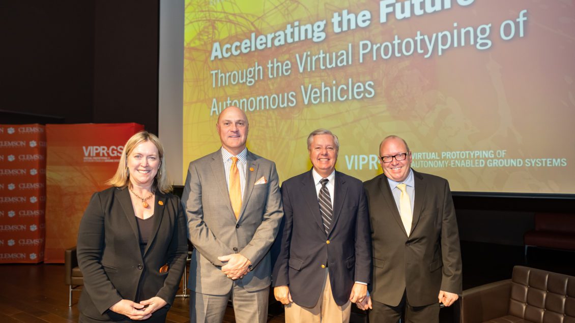 A woman and three men stand in front of a giant screen that reads Accelerating the Future Through the Virtual Prototyping of Autonomous Vehicles. This is for the Clemson Army Partnership and includes Angie Leidinger, President Jim Clements, U.S. Senator Lindsay Graham, U.S. Army Chief Scientist David Gorsich