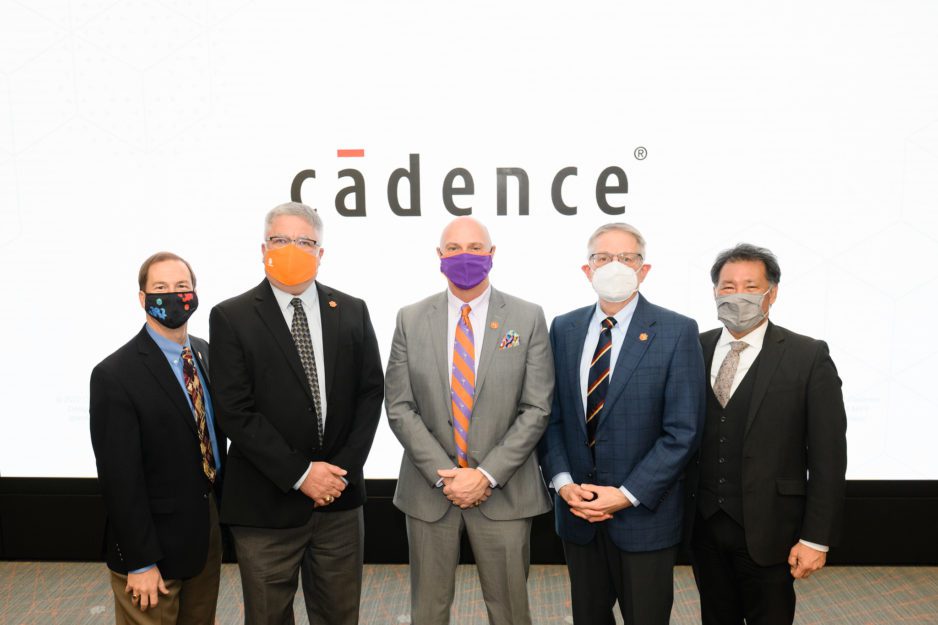 Four white men and one Asian man wearing suits and face masks, including the President of Clemson University and Cadence software executives. One is a Clemson alum. They are standing infront of a backdrop with the Cadence logo on it.