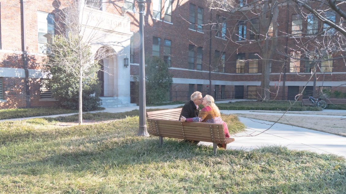 A couple shares a kiss on a bench outside Sirrine Hall.