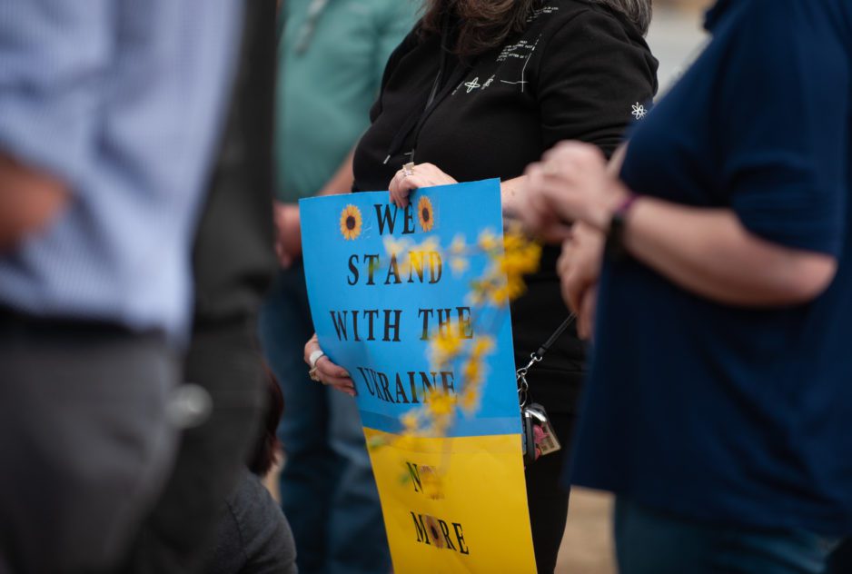 A blue and yellow sign reads "We stand with Ukraine" and is held by two sets of women's hands. They are standing on Bowman Field for the March 6, 2022, Clemson Stands With Ukraine rally.