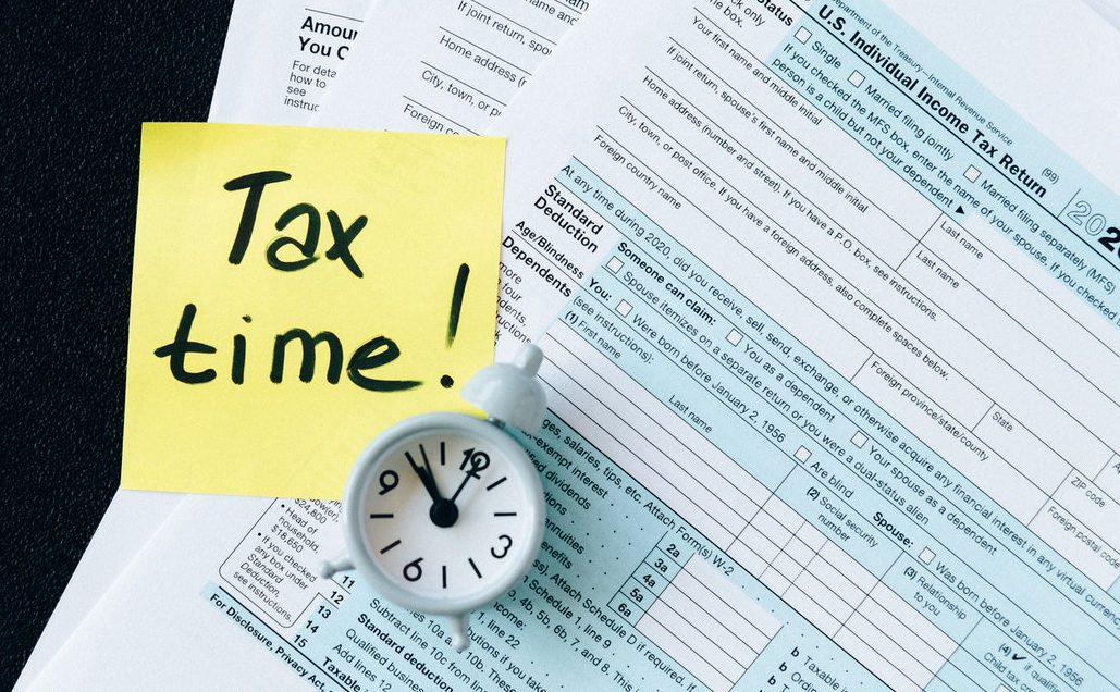 tax filing papers stacked on top of each other, with a clock and a sticky note that reads "tax time!"