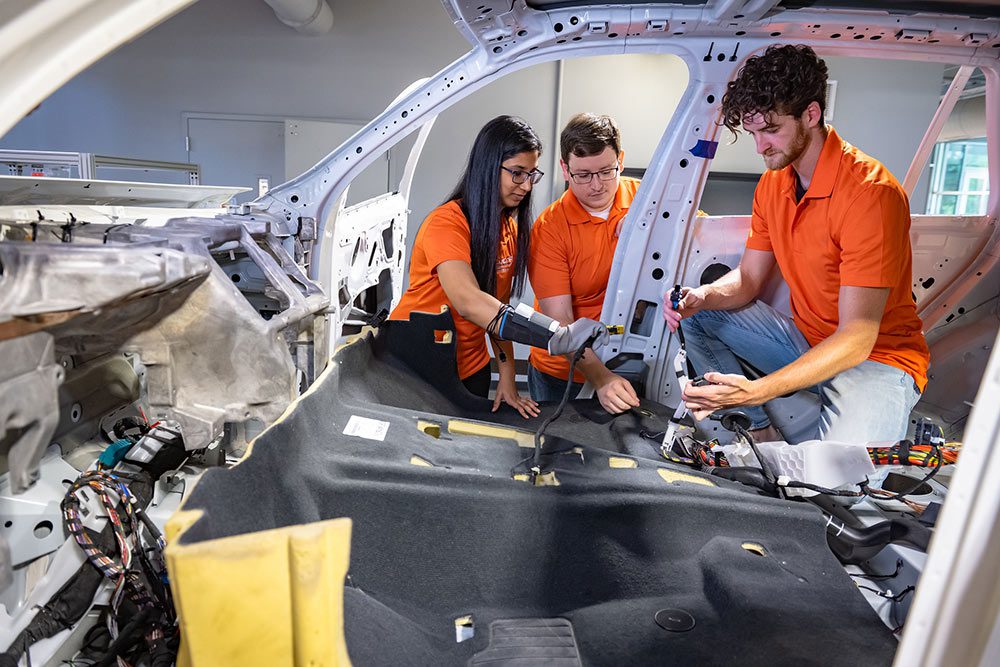 Three students work on a car in the assembly phase.
