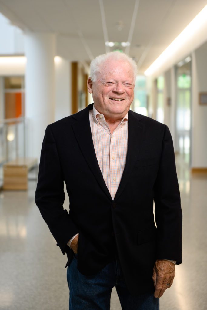 Portrait of Robert E. (Bobby) McCormick, ‘72, professor emeritus and former dean of the College of Business standing in the hallway of an academic building
