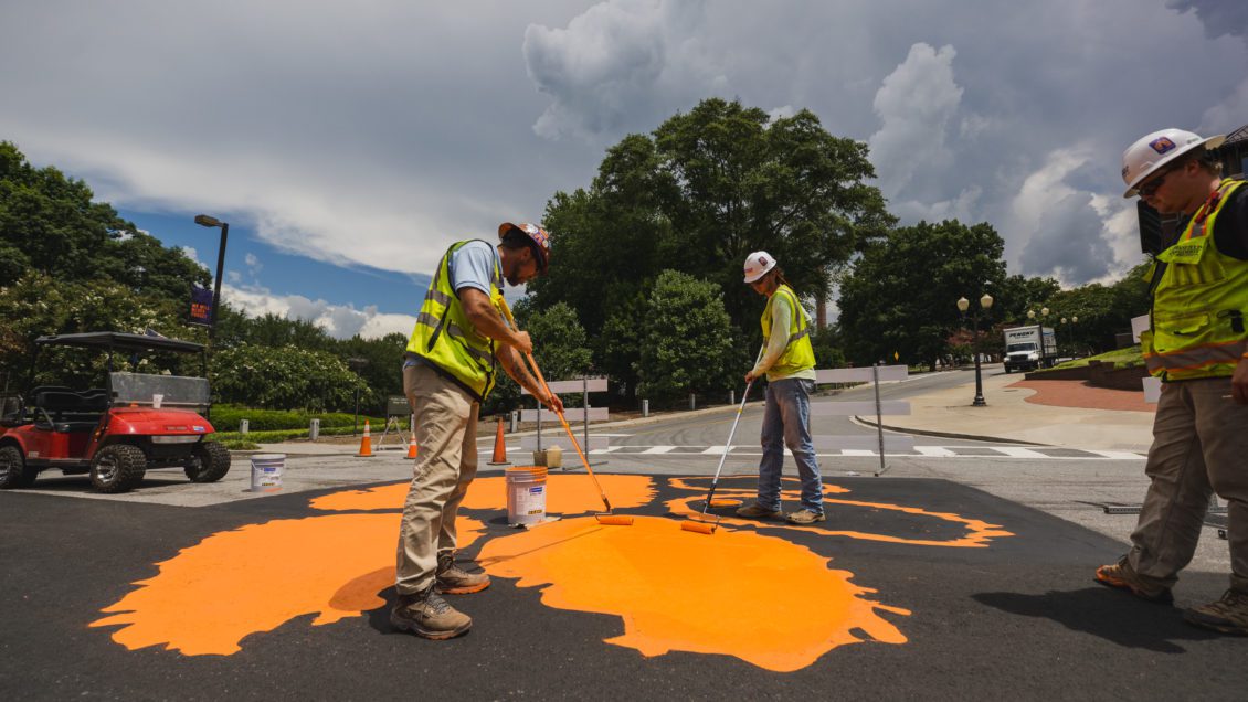 Two construction workers repaint an orange Tiger Paw on the road in front of Memorial Stadium.
