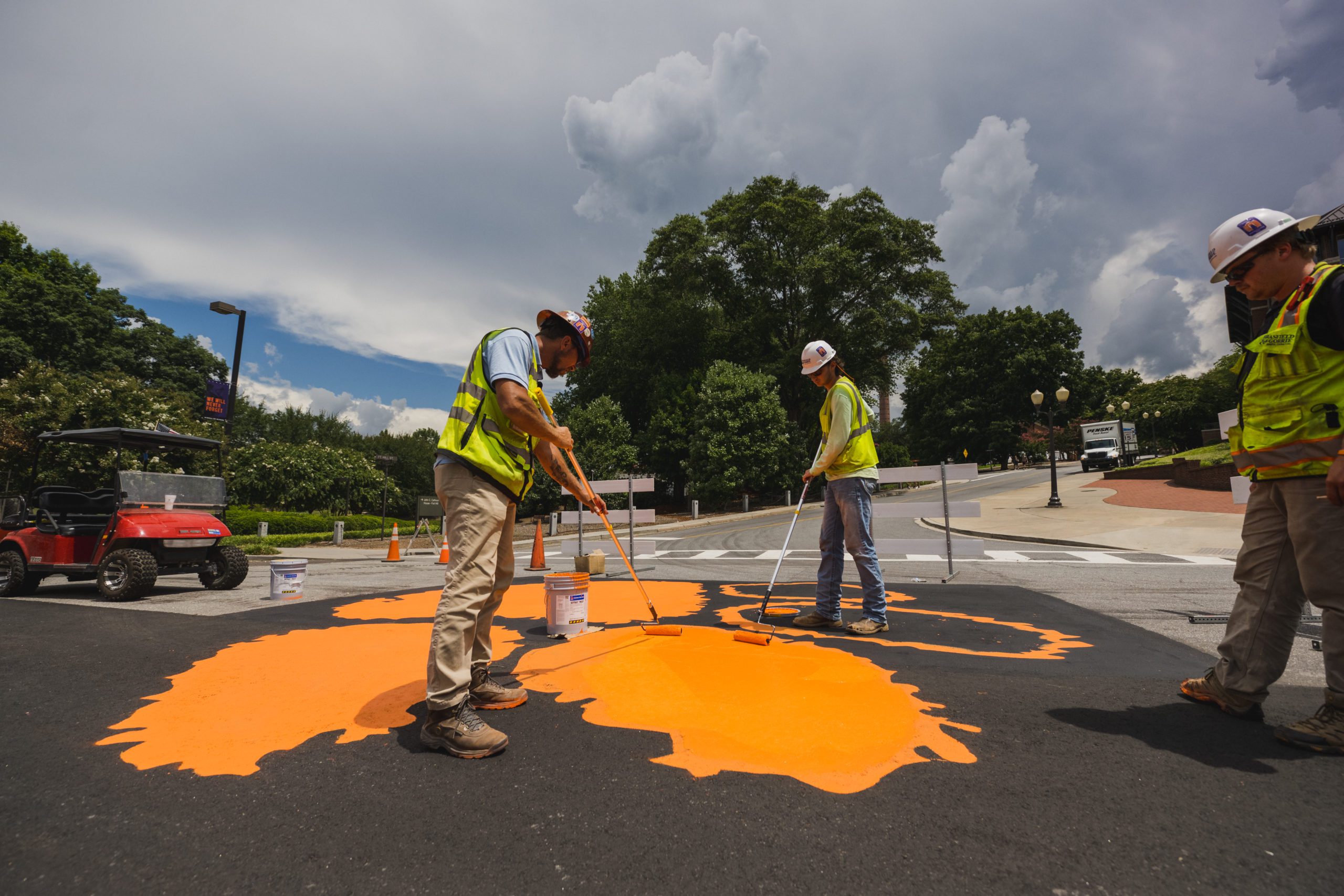 Two construction workers repaint an orange Tiger Paw on the road in front of Memorial Stadium.