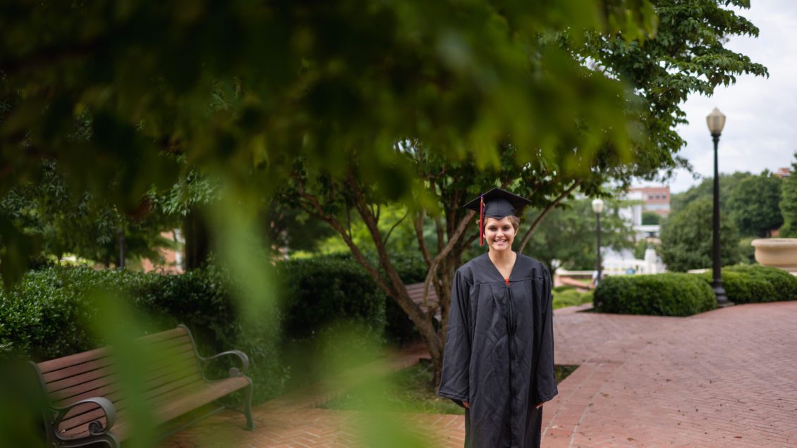 Student in cap and gown standing under a tree