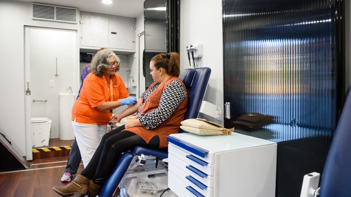 A Clemson-orange wearing nurse treats a patient inside a mobile health unit.