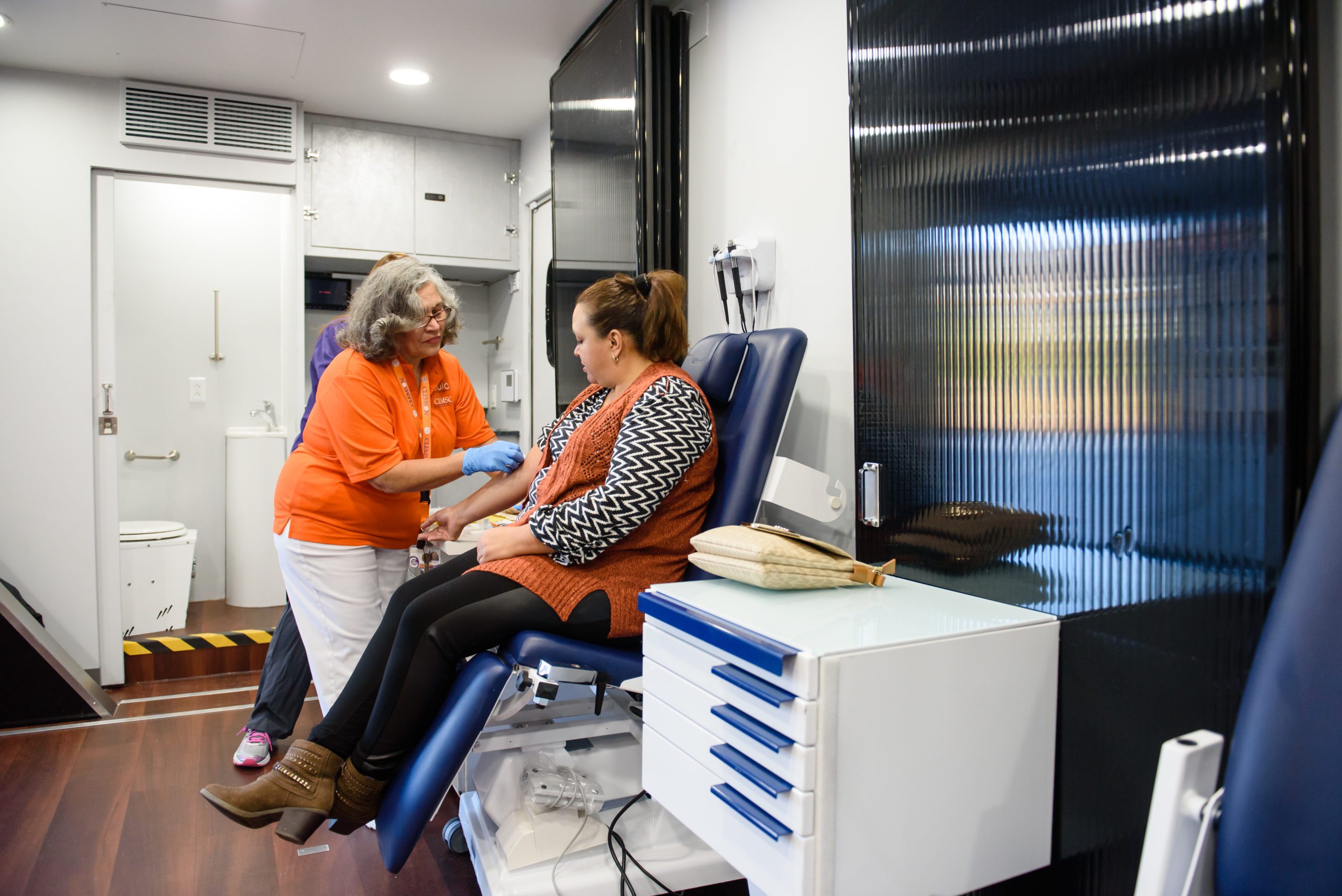 A Clemson-orange wearing nurse treats a patient inside a mobile health unit.