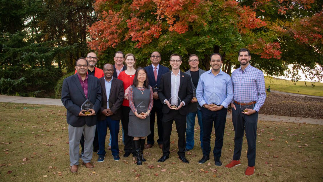 Eleven faculty members standing in front of a tree posing with their award for excellence in teaching, research and enhancing the Clemson Experience.