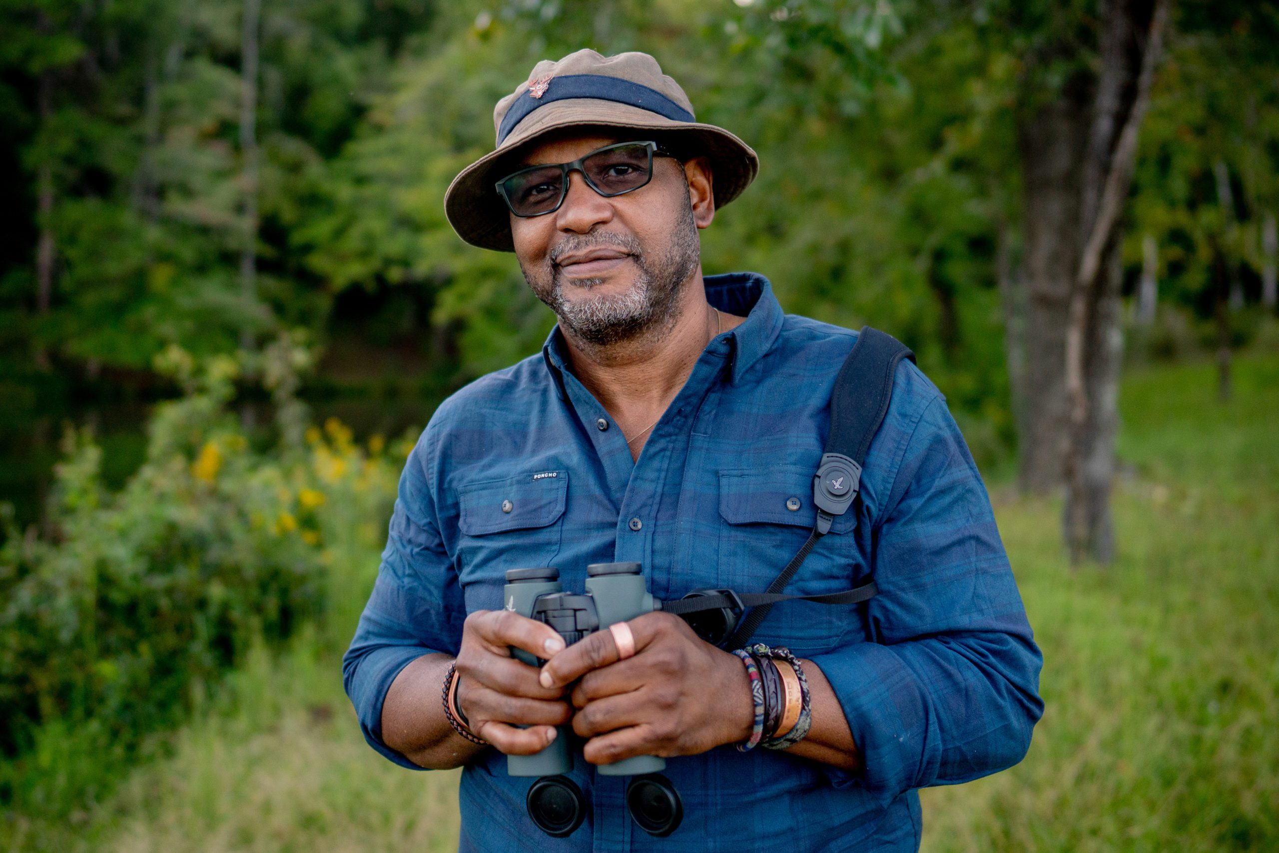 Environmental portrait of J. Drew Lanham, Clemson Alumni Distinguished Professor of Wildlife Ecology, standing in a wooded area holding binoculars. 